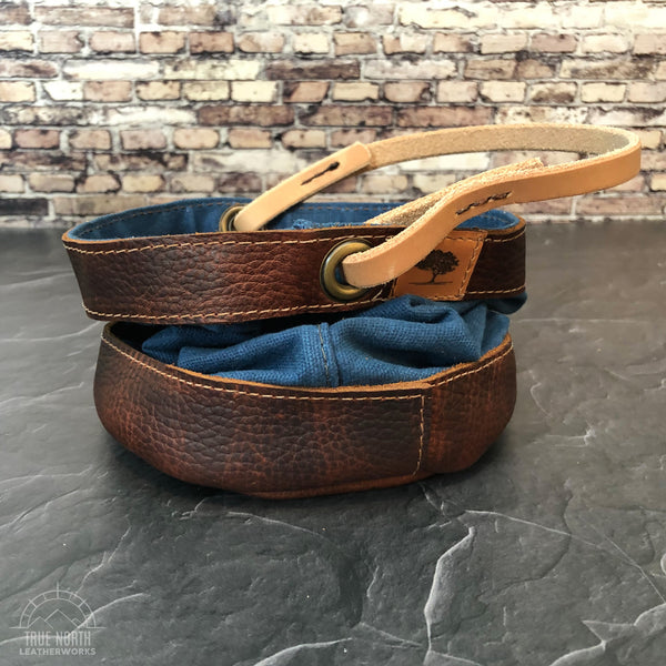 Scrunched down handmade blue waxed canvas and brown leather bucket sitting on a black surface