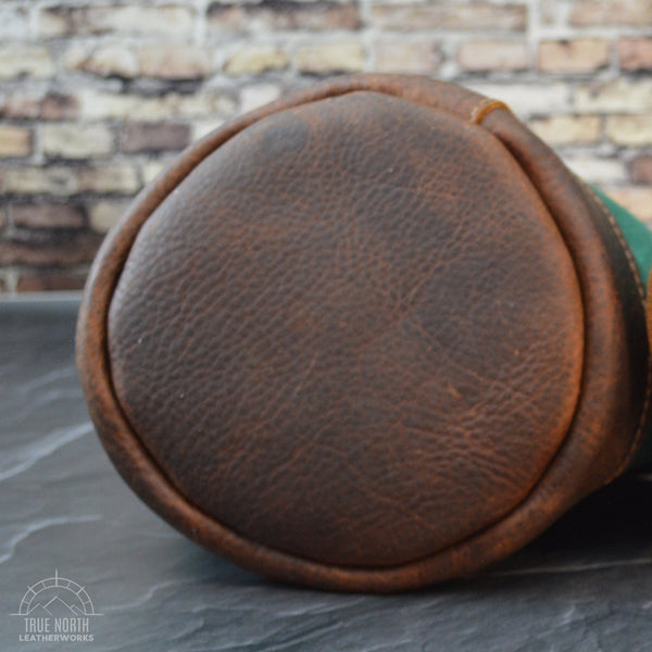The round brown leather bottom of a waxed canvas and leather bucket bag